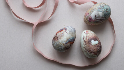 Three Easter eggs in light pink pastel colors lie on a table next to a pink cotton ribbon