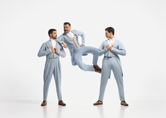 Portrait with three men wearing elegant clothes jumping and dancing over white background.