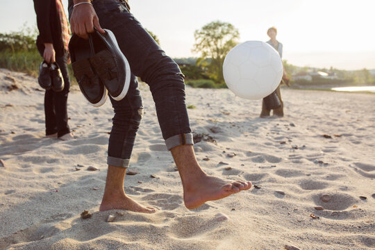 Low section of people kicking ball on beach
