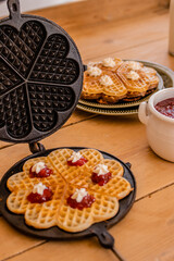 An antique waffle iron with a freshly baked waffle and a dish with freshly baked waffles