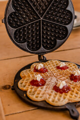 An antique waffle iron with a freshly baked crispy waffle, decorated with cream and raspberry jam