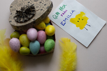 A heart full of Easter egg candies, colored feathers and an Easter card made by a child