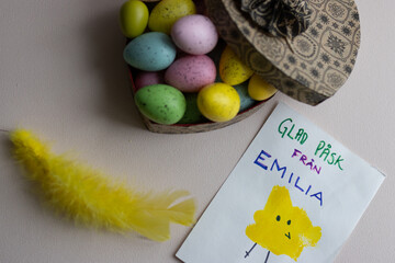 A heart full of Easter egg candies, colored feathers and an Easter card made by a child