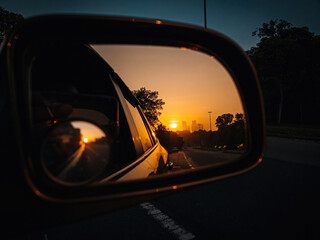 Reflection of golden sunrise in wing mirror of a car at the roadside in Malaysia.