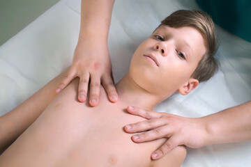 Fototapeta na wymiar Session of craniosacral therapy, cure of teen boy spine by a doctor therapist. Boy is lying on couch. Craniosacral therapist touches boy on collarbone and shoulders to cure and correct spine posture.