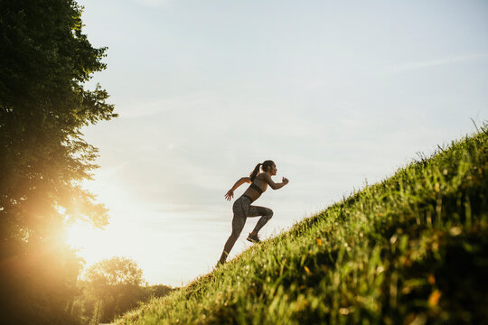 Young woman running up hill in sunlight