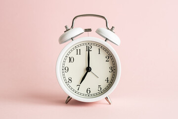 かわいいピンクの背景に白い目覚まし時計　女性らしい時間のイメージ写真