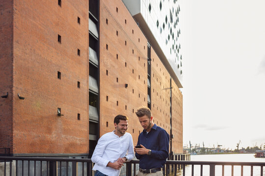 Men standing on bridge near Elbphilharmonie and looking at phone