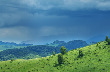 Fototapeta na wymiar Mountains and hills in stormy weather, contrasting light, summer greenery of forests and meadows