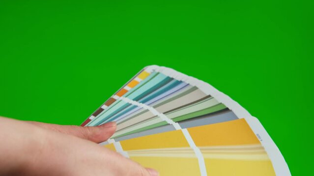 Hands choose the color using the sample swatch on blank green screen mock up. Creative designer using Color Guide with color chart samples on Chromakey green background. Colors palette fan, catalogue