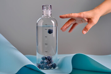 A woman's hand reaches for a glass bottle with blueberries.