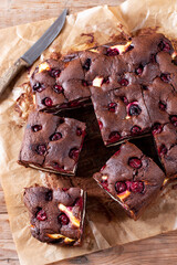 Chocolate brownie with cherries and cheese layer. Many pieces of chocolate dessert on a wooden board