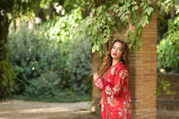 Beautiful young woman in a typical Moroccan red suit, embroidered with gold and silver threads, posing next to a brick column with a vine. Concept beauty, ethnicity, typical suits, Marrakech, Arab.
