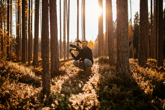 Man crouching in forest holding camcorder