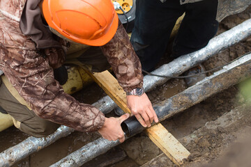 Worker in helmet repairs communal water pipe in trench on street. Work of public utilities to eliminate accident. Replacement of old water supply pipes. Authentic workflow. Real people..