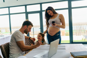 father sitting at the desk and helps his daughter with homework, while the mother with her exposed...