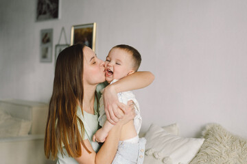Home portrait of a baby boy with mother on the bed relaxing and playing in the bed at the weekend together, lazy morning, warm and cozy scene. Mom holding and kissing her child. Mother day concept