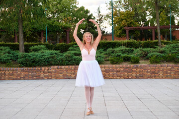 Mature smiling woman dancing ballet in a park at street.
