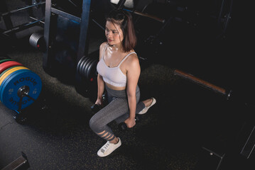 Fototapeta na wymiar A young asian woman does a set of dumbbell lunges. Working out legs at the gym.
