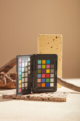 A color checker placed on a stone podium in rectangle shape, displayed with tree branch on beige background