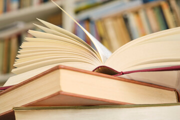 Open book or textbook on a pile of closed books in front of a bookcase in a library. Education learning concept. Image with selective focus.	