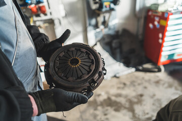 closeup shot of mechanic's hands holding an old broken clutch at the car shop, car repair concept....