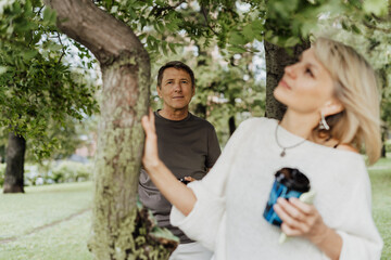 An adult mature happy couple in love hugging outdoors in city park. A blonde caucasian man and woman spend time together and drinking coffee. Senior wife and husband walking outside