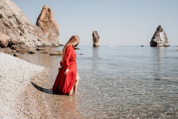 Fototapeta na wymiar Woman travel sea. Happy tourist in red dress enjoy taking picture outdoors for memories. Woman traveler posing on the rock at sea bay surrounded by volcanic mountains, sharing travel adventure journey