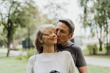 An adult mature happy couple in love hugging outdoors in city park. A blonde caucasian man and woman spend time together and drinking coffee. Senior wife and husband walking outside