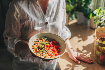 Young woman eating healthy food sitting in the beautiful interior with green flowers on the background
