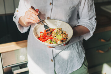 Young woman eating healthy food sitting in the beautiful interior with green flowers on the background