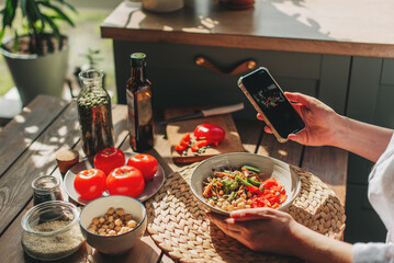 Woman taking photo of fresh, raw, sliced vegetables on the plate with smartphone. Food blogger using phone to capture meal. Lifestyle trend - posting and sharing food pictures on social media.