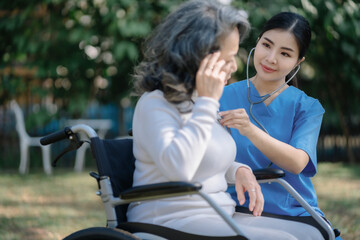Obraz premium Nurse with stethoscope examining patient sitting in a wheelchair outdoor.