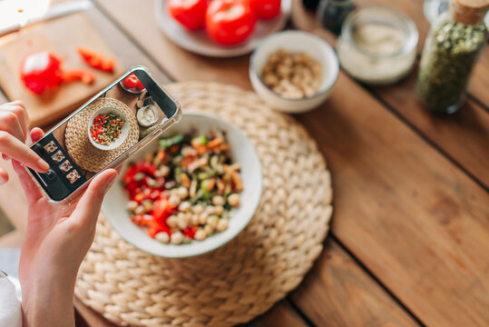 Woman taking photo of fresh, raw, sliced vegetables on the plate with smartphone. Food blogger using phone to capture meal. Lifestyle trend - posting and sharing food pictures on social media.