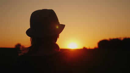 A lonely woman in a hat looks at the sunset. Back view. Dreaming and planning a concept