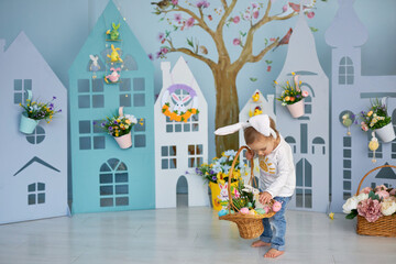 Baby girl celebrate Easter. Funny happy kid in bunny ears playing on Easter egg hunt. Family home decoration, colorful Easter eggs and flowers. Home decoration and flowers