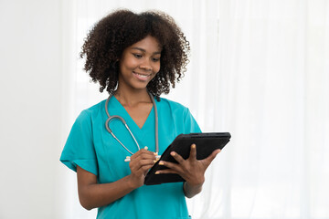 Happy young female doctor wearing blue scrubs uniform and stethoscope and standing holding digital tablet in hospital. African American young nurse standing and smiling on white background