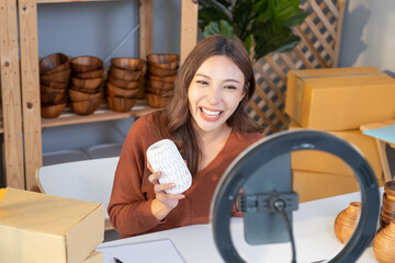 Young Asian female entrepreneur smile while talking on the phone and check customer order from online shopping inside of home office. New small business start up trend with online marketing.