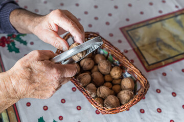 Hände eines Alten Mann Opa Rentner knackt mit einem Nussknacker aus Metall eine Walnuss an einem...