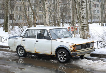 Obraz na płótnie Canvas An old white rusty car is parked in the courtyard of a residential building, Dybenko Street, St. Petersburg, Russia, March 2023