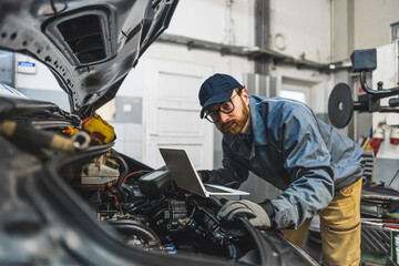 Auto mechanic uses laptop while conducting diagnostics test. Modern car service. Computer...