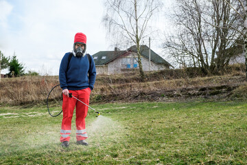 Farmer spraying pesticide on lawn field wearing protective clothing. Treatment of grass from weeds...