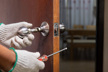 Locksmith on wood door with screwdriver for repair or fix silver knob..