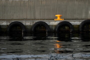 Vibrant orange steel bollard at a dock, with black tiers partway submerged in the water