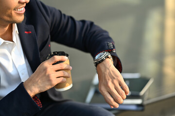 Cropped shot of young businessman sitting outdoors waiting for meeting and checking time looks at wristwatch