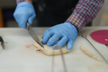 Cook wearing hygienic gloves cuts pita bread with a knife on a cutting board in a commercial kitchen