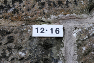 Close Up of Numbers 12 and 16 on Plaque Attached to Rough Textured Stone Wall 