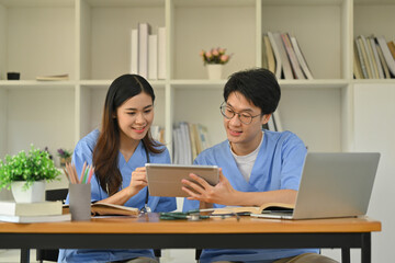Male and female nurse wearing blue scrubs talking about patients diagnosis, checkup results on digital tablet