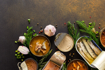 Different open tin cans with canned fish among spices and herbs on a brown background, canned...