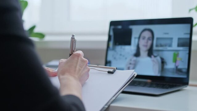Talking young woman on laptop screen and female with clipboard making notes, video chat